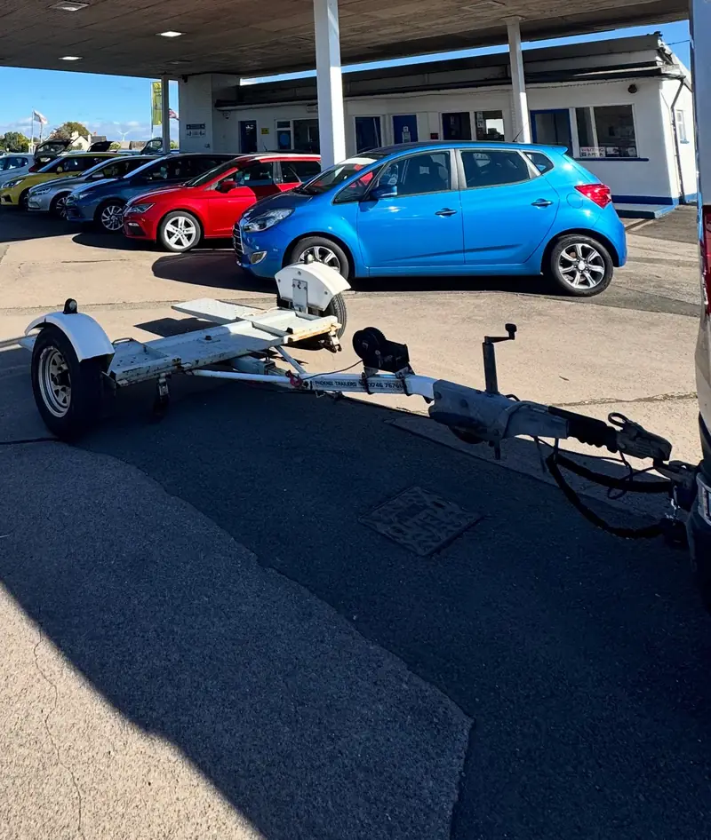 Empty tow dolly hitched up on a garage forecourt, ready to collect a car